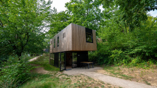 Moderne Woodland Lodge 6 met houten bekleding, grote ramen en omgeven door weelderig groen bos.