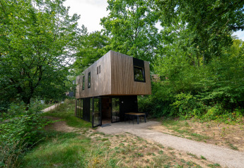 Moderne Woodland Lodge 6 med træfacade og store vinduer, omgivet af grønne træer og natur.