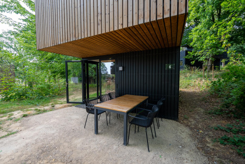 Mesa exterior con seis sillas en Woodland Lodge 6 en Gulpen, Países Bajos, rodeada de vegetación.