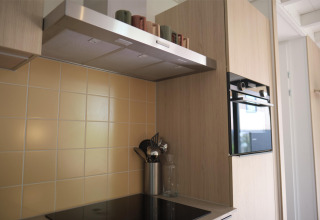 Moderne keuken met keramisch vuur, oven, dampkap en beige tegels in Woodland Lodge 6 te Gulpen.