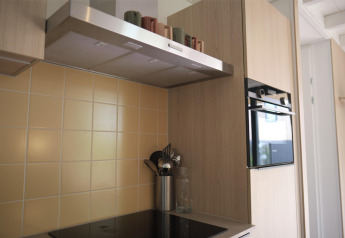 Moderne Küche mit Kochfeld, Backofen, Dunstabzugshaube und beiger Fliesenwand in Woodland Lodge 6, Gulpen.