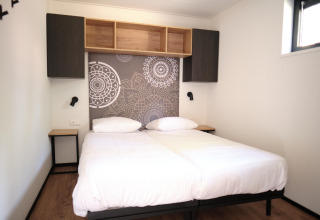 Habitación con dos camas individuales, arte de pared moderno y armarios en Timber Lodge 4 en Gulpen, Países Bajos.