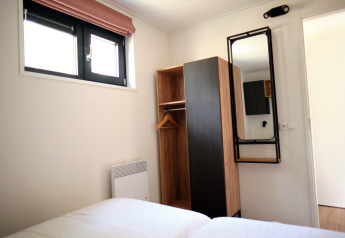 Dormitorio en Timber Lodge 4 en Gulpen, Países Bajos, con armario, espejo de pared y ventana.