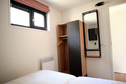 Slaapkamer in Timber Lodge 4 te Gulpen, Nederland, met kast, wandspiegel en bovenliggend raam.