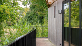 Balkon van Timber Lodge 4 met houten gevel, zwart hek en uitzicht op groene bomen in de natuur.