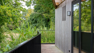 Balcone della Timber Lodge 4 con rivestimento in legno, parapetto nero e vista su alberi verdi.