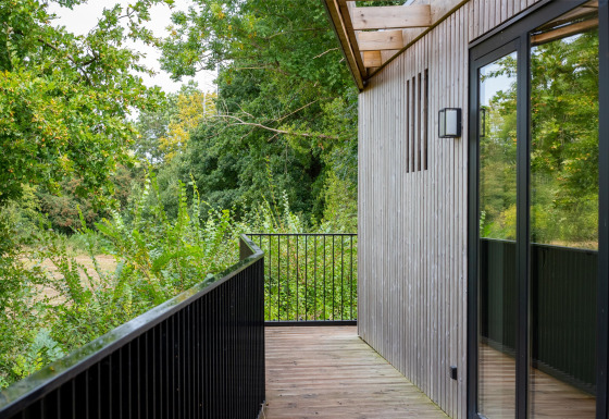 Balkon von Timber Lodge 4 mit Holzverkleidung, schwarzem Geländer und Blick auf grüne Bäume.