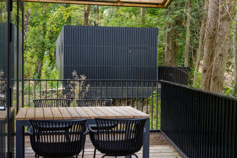 Terraza de madera con mesa y sillas en Timber Lodge 4 en Gulpen, Países Bajos, rodeada de árboles.