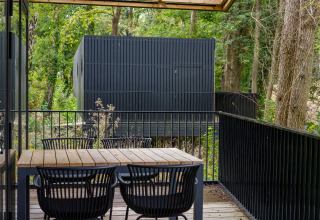 Holzterrasse mit Tisch und Stühlen bei Timber Lodge 4 in Gulpen, Niederlande, von Bäumen umgeben.