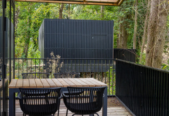 Terraza de madera con mesa y sillas en Timber Lodge 4 en Gulpen, Países Bajos, rodeada de árboles.
