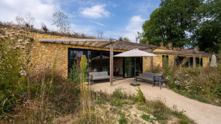 Außenansicht der Hillside Comfort 4 Lodge mit Natursteinwänden, Terrasse und wilder Vegetation.