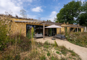 Buitenaanzicht van Hillside Comfort 4 lodge met stenen gevels, tuinmeubilair en wilde planten rondom.