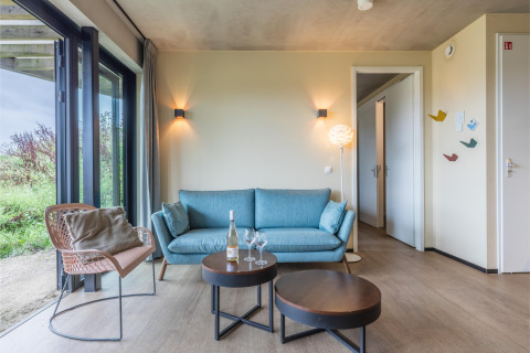 Salón moderno en la Hillside Royal 4 de Gulpen, Países Bajos, con sofá azul y grandes ventanales.