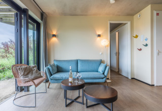 Salón moderno en la Hillside Royal 4 de Gulpen, Países Bajos, con sofá azul y grandes ventanales.