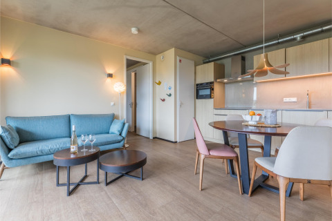 Sala moderna en lodge con sofá azul, mesa de comedor y cocina en Hillside Royal 4 en Gulpen, Países Bajos.