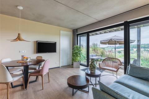 Luminoso y moderno salón en la cabaña Hillside Royal 4 en Gulpen, Países Bajos, con vistas a la terraza y campo.