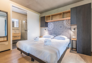 Dormitorio moderno con cama doble, pared decorada y baño en suite en Hillside Royal 4, Gulpen.