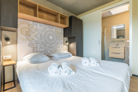 Camera di lodge moderna con letto doppio, parete decorata, asciugamani freschi e vista sul bagno.