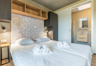 Camera di lodge moderna con letto doppio, parete decorata, asciugamani freschi e vista sul bagno.