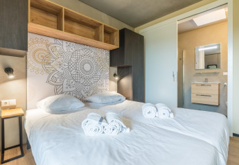Habitación moderna en lodge con cama doble, pared decorativa, toallas limpias y acceso al baño.