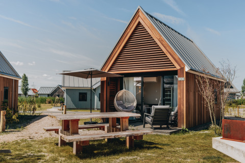 Tiny House 2 at Nieuwvliet-Bad in the Netherlands with wooden siding, patio furniture, and outdoor picnic table.