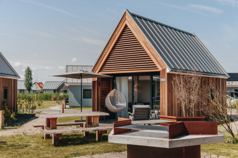 Moderne Tiny House 2 med træfacade og terrasse ved Nieuwvliet-Bad, Holland, udendørs møbler og grill.