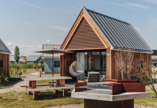 Moderne Tiny House 2 med træfacade og terrasse ved Nieuwvliet-Bad, Holland, udendørs møbler og grill.