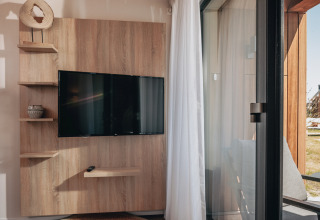 Flat-screen TV mounted on a wooden wall with shelves in Tiny House 2 at Nieuwvliet-Bad, Netherlands.