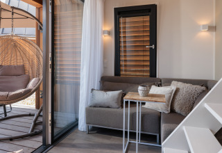 Moderne tiny house-stue med hyggelig sofa, lille bord, hængestol og vindue på Nieuwvliet-Bad, Holland.