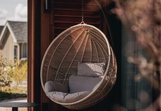 Hængende kurvestol med puder på verandaen af Tiny House 2 ved Nieuwvliet-Bad i Holland, sollys skinner igennem.