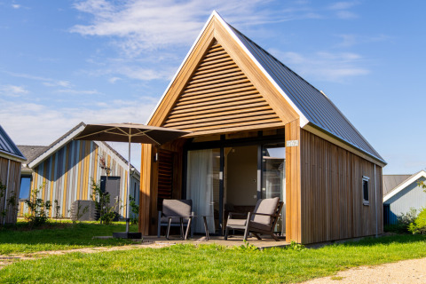 En moderne Tiny House 2 ved Nieuwvliet-Bad i Holland med terrasse, parasol og havemøbler om sommeren.