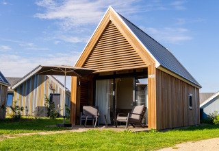 En moderne Tiny House 2 ved Nieuwvliet-Bad i Holland med terrasse, parasol og havemøbler om sommeren.