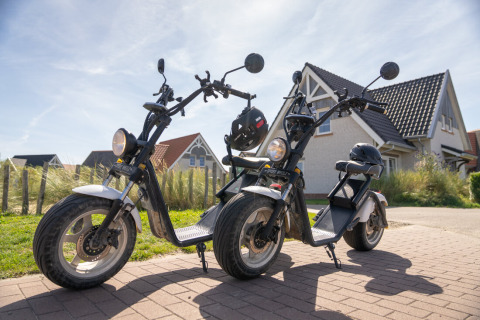 Zwei Elektroscooter mit Helmen stehen vor einem Haus in Nieuwvliet-Bad, Zeeland, Niederlande.