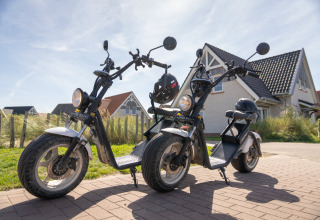 Dos scooters eléctricos con cascos están aparcados frente a una casa en Nieuwvliet-Bad, Zelanda, Países Bajos.
