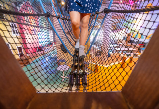 Kind überquert eine Kletternetzbrücke in einem bunten Indoor-Spielbereich in Nieuwvliet-Bad, Zeeland.