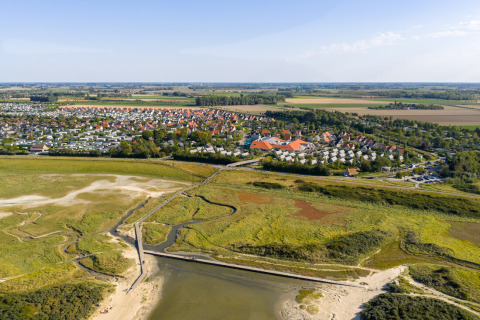 Luftfoto af ferieparken Nieuwvliet-Bad i Zeeland, Holland, omgivet af grønne marker og strand.
