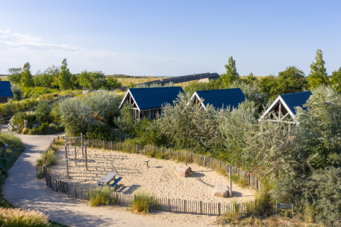 Feriehytter med blå tage omgivet af grønt og legeplads i sand ved Nieuwvliet-Bad, Zeeland, Holland.