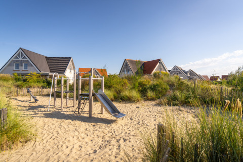 Legeplads med rutsjebane og sand omgivet af sommerhuse ved Nieuwvliet-Bad feriepark i Zeeland, Holland.