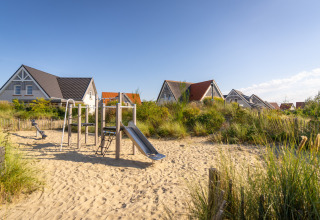 Playground with slide and sand surrounded by holiday homes at Nieuwvliet-Bad holiday park in Zeeland, Netherlands.