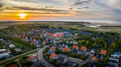 Luftfoto af ferieparken Nieuwvliet-Bad i Zeeland, Holland, med farverige hustage og solnedgang ved havet.
