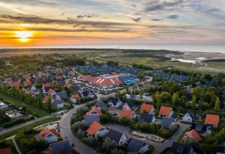 Aerial view of Nieuwvliet-Bad holiday park in Zeeland, Netherlands, with colorful houses and a scenic sunset.