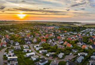 Aerial view of Nieuwvliet-Bad holiday park in Zeeland, Netherlands at sunset with houses and green spaces.