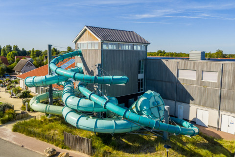 Large, twisting water slide at the Nieuwvliet-Bad holiday park in Zeeland, Netherlands, set among buildings.