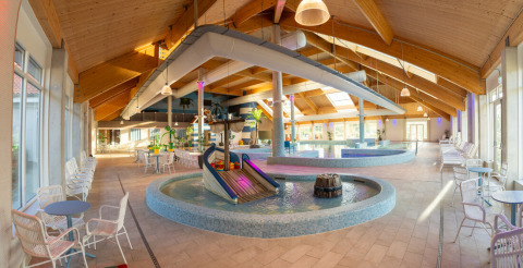 Indendørs swimmingpoolområde med rutsjebane, borde og stole ved Nieuwvliet-Bad feriepark i Zeeland.