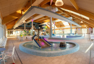 Indendørs swimmingpoolområde med rutsjebane, borde og stole ved Nieuwvliet-Bad feriepark i Zeeland.