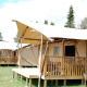Reihe von Dreamer Safari-Zelten mit Holzveranda, umgeben von grünen Bäumen unter klarem Himmel.