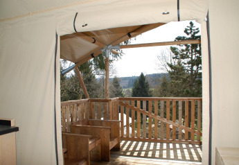 Blick aus dem Safari-Zelt Dreamer in Petite Suisse, Belgien, mit Holzterrasse und Waldlandschaft.