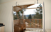 Vue depuis la tente safari Dreamer à Petite Suisse, Belgique, montrant une terrasse en bois et la forêt.