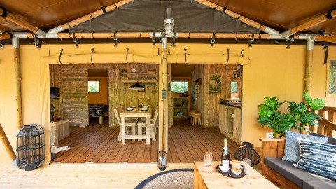 Vista interior de la tienda safari Dreamer en Petite Suisse, Bélgica, con terraza de madera y sofá acogedor.