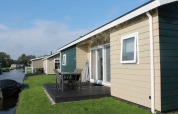 Moderne lodge Fuut 4 med terrasse ved vandet, udendørs spisning og grønne områder under blå himmel.